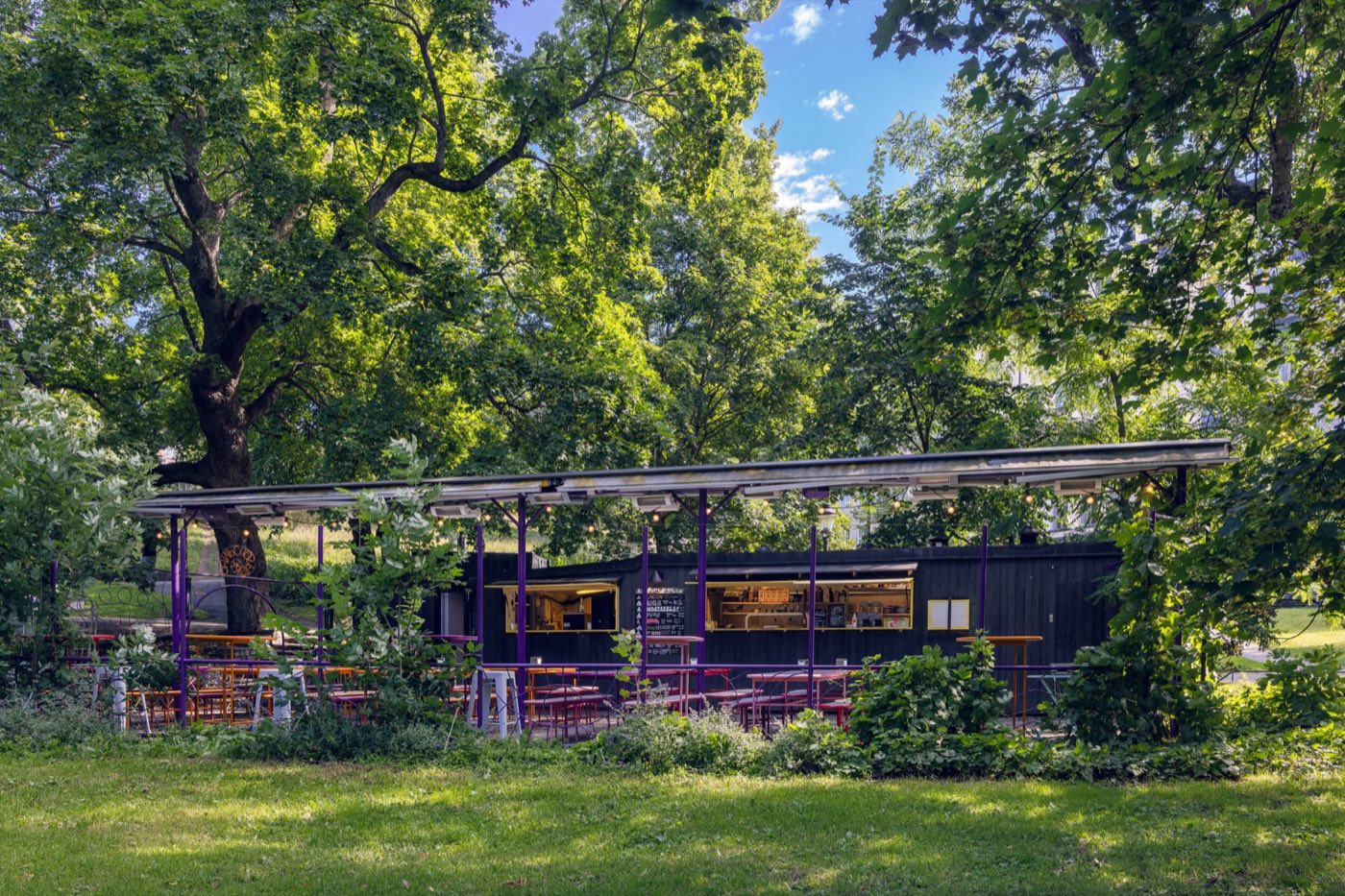 Omnipollos Flora i Humlegården — en svart paviljong med uteservering under trädkronorna.